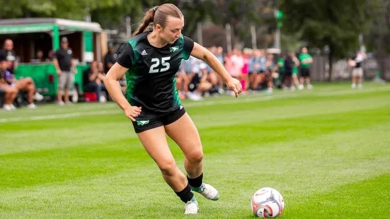 Player in black uniform kicking soccer ball on field