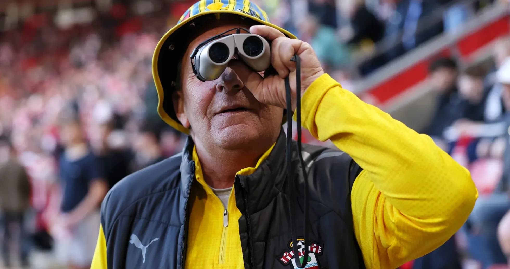 Fan wearing binoculars and yellow outfit at stadium