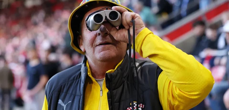 Fan wearing binoculars and yellow outfit at stadium