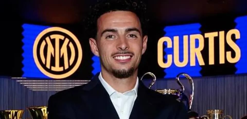 Player smiling with trophies and club logo backdrop