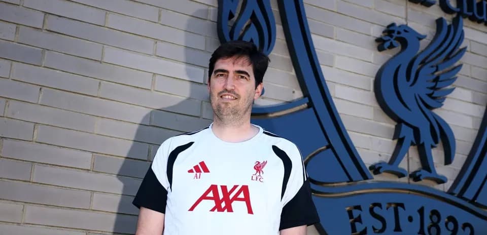 Man in Liverpool FC training shirt near club logo
