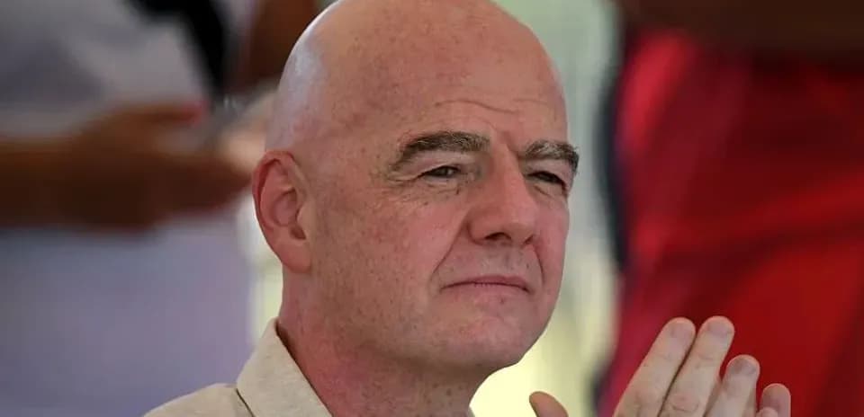 Man with bald head seated, hands clasped together