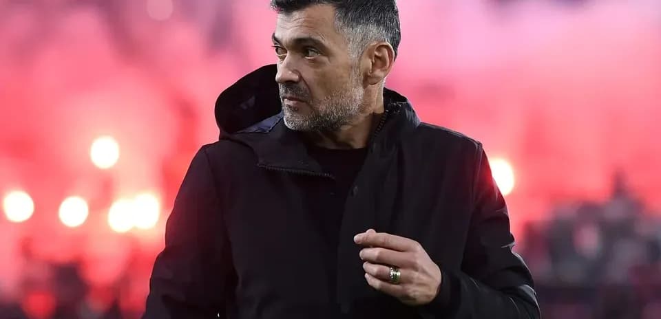 Coach observing match with stadium smoke in background