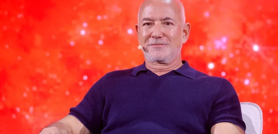 Man seated on stage with a red background