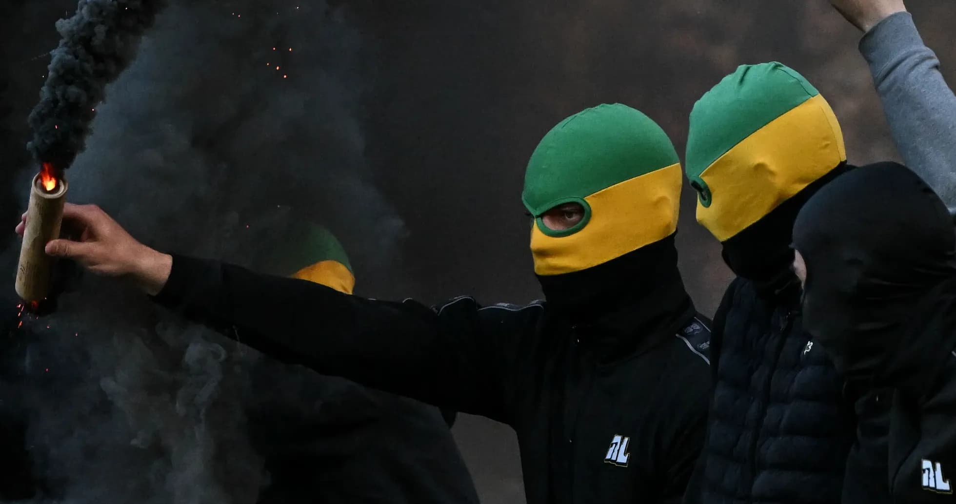 Masked individuals holding a flare in smoky atmosphere