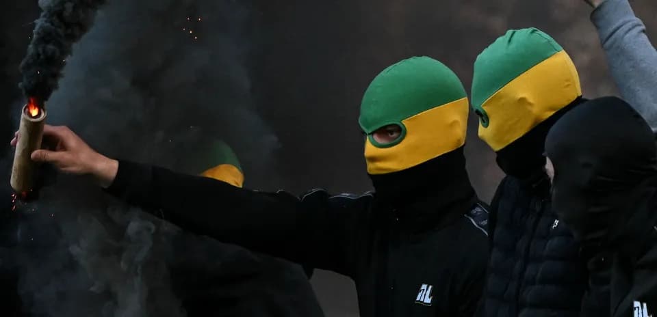 Masked individuals holding a flare in smoky atmosphere