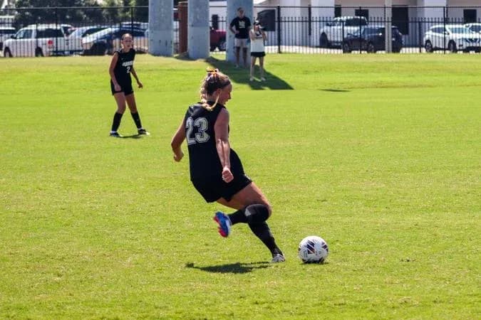 Player in black kicking soccer ball on field