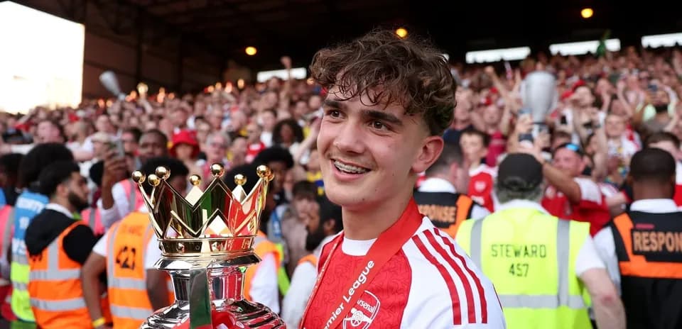 Player holding Premier League trophy with fans celebrating