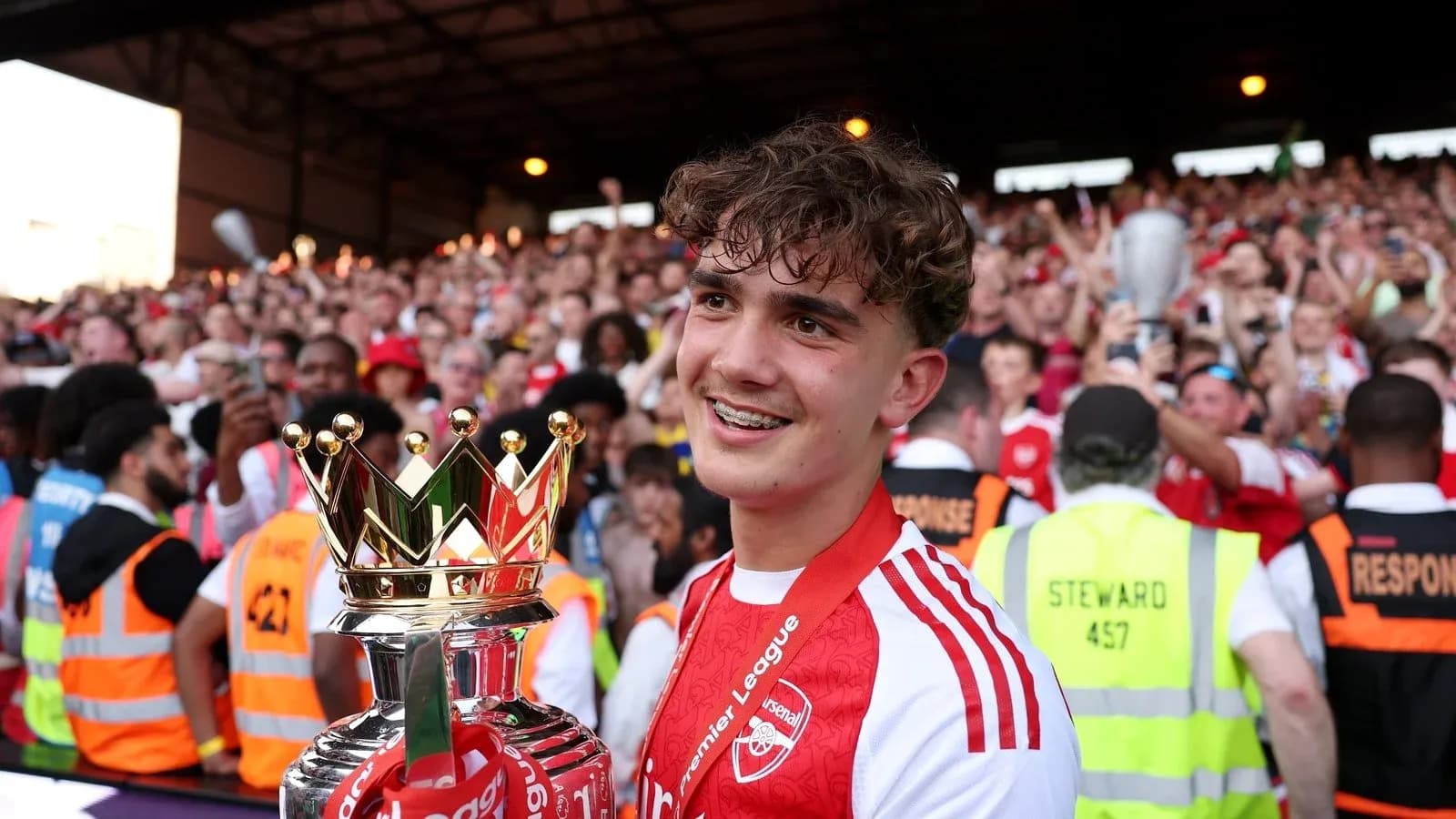 Player holding Premier League trophy with fans celebrating