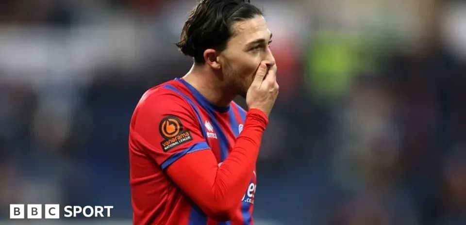 Player in red and blue kit touching face during match
