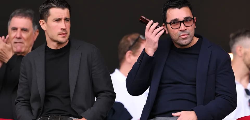 Two men seated in a stadium, one on phone
