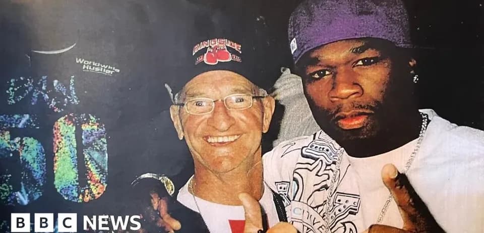 Two men posing together, one wearing a cap