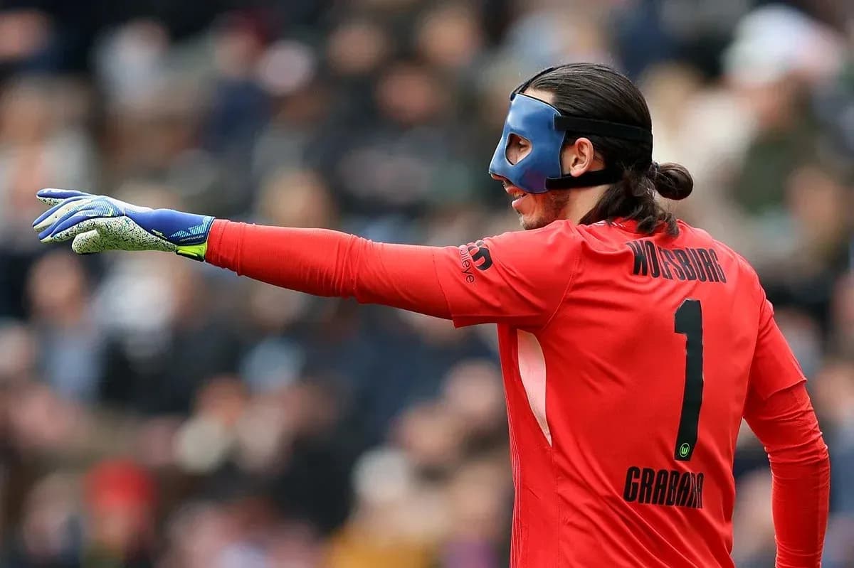 Goalkeeper in red kit directing play with gloved hand