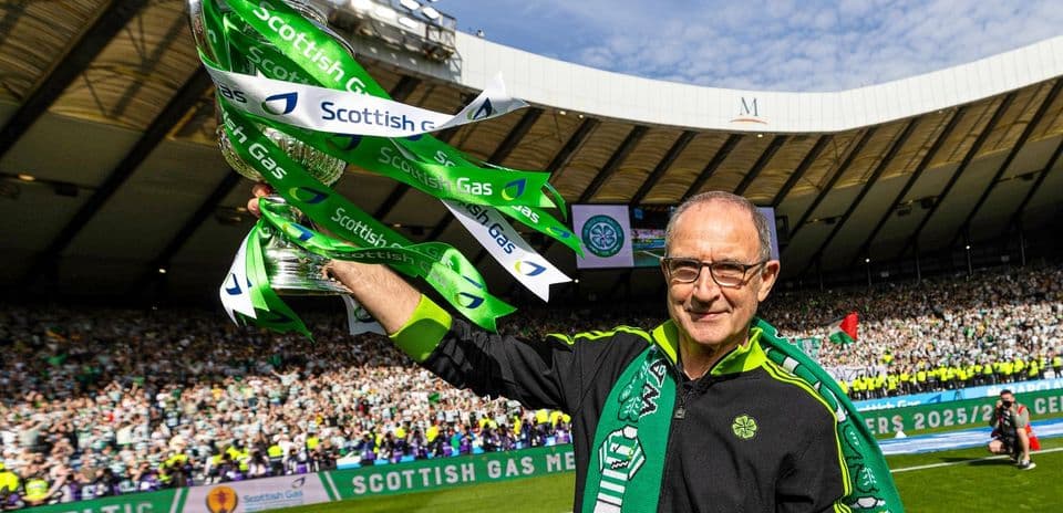 Man holding trophy with Celtic fans celebrating in background