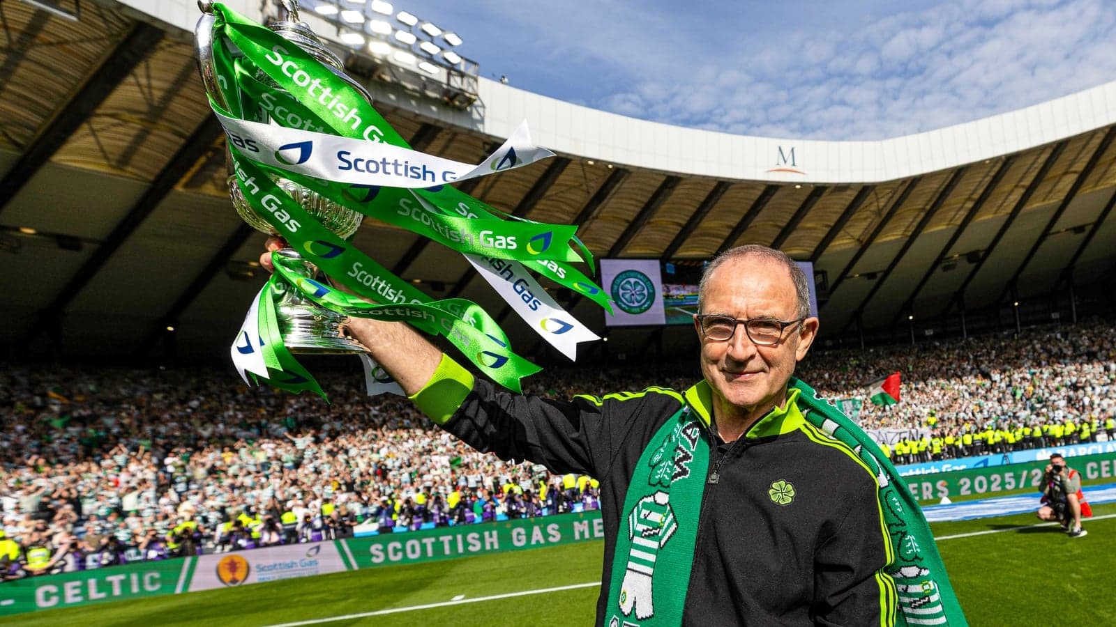 Man holding trophy with Celtic fans celebrating in background