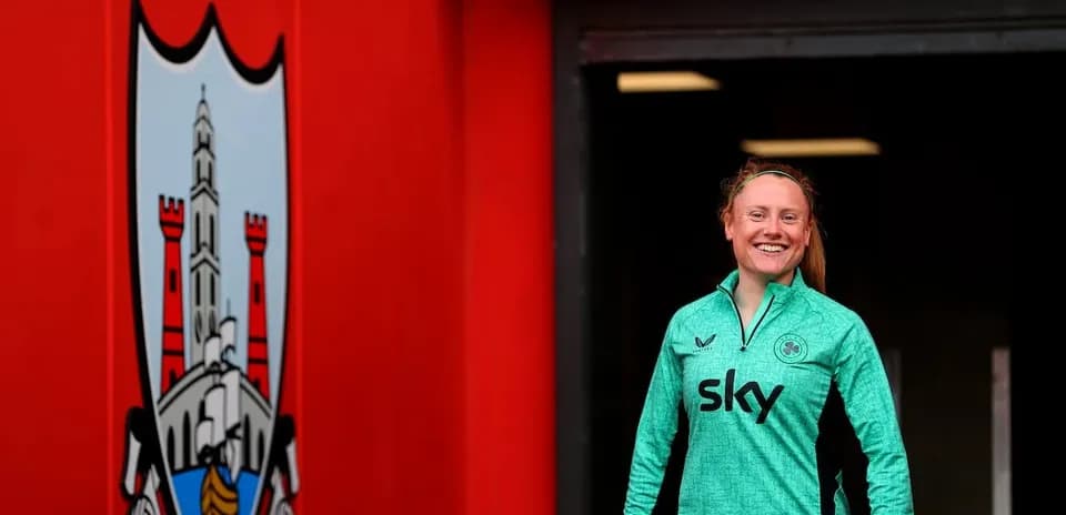 Player in green kit smiling near club logo