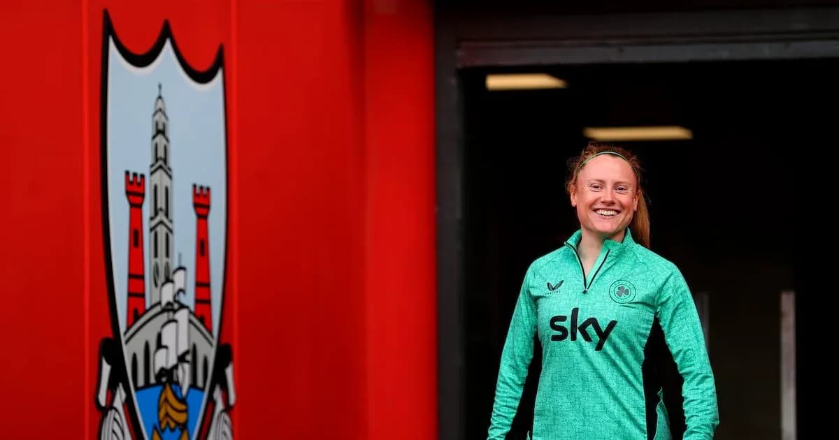 Player in green kit smiling near club logo