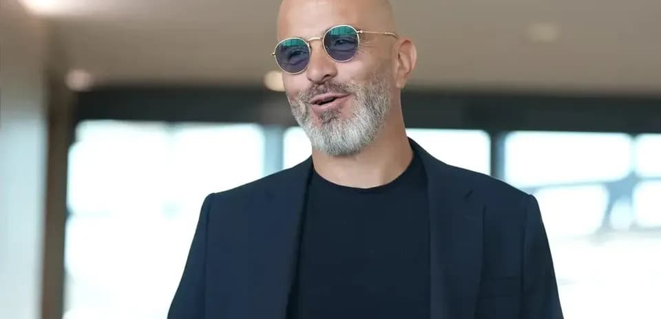 Man in sunglasses smiling indoors with blurred background