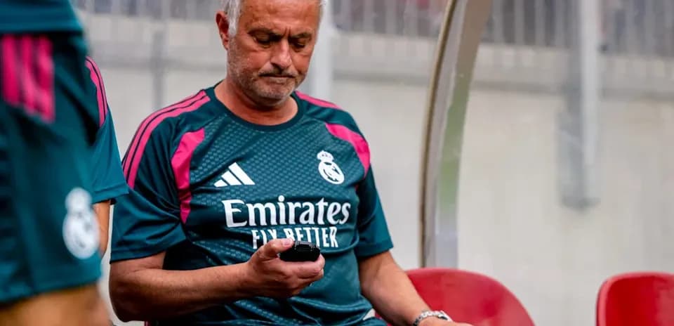 Manager seated on bench, using phone during match