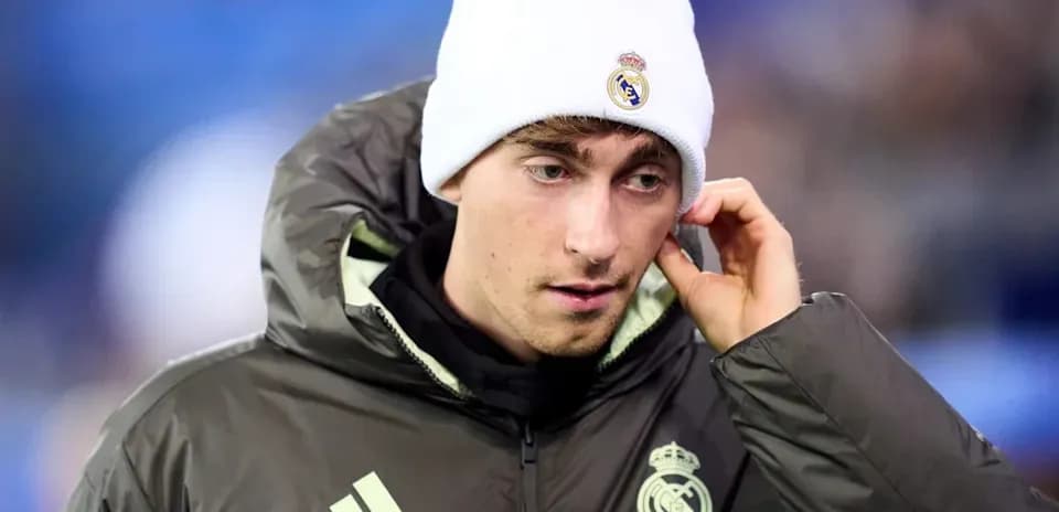 Player wearing Real Madrid jacket and beanie on sidelines