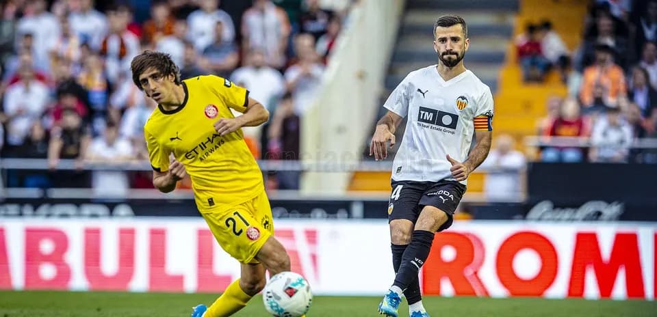 Valencia player challenges Girona opponent for the ball