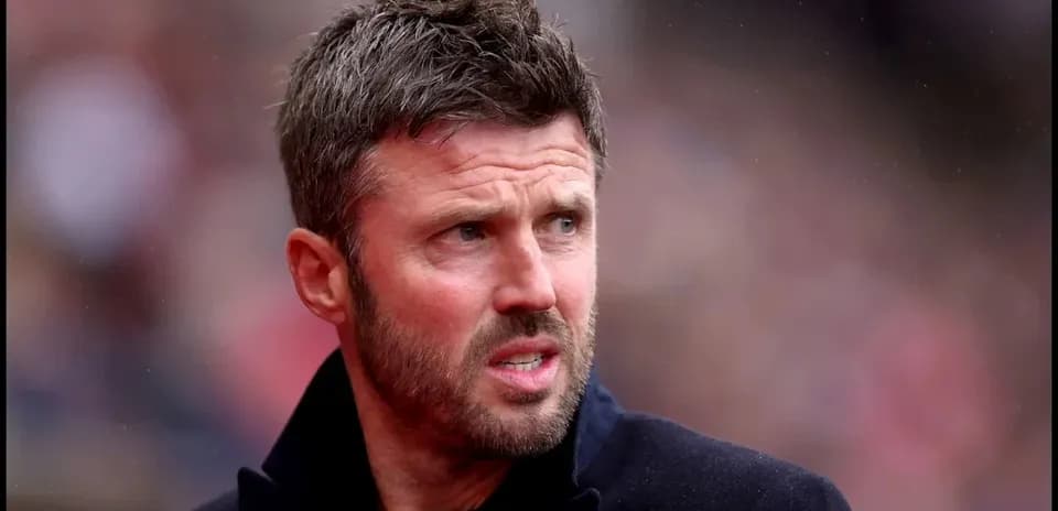 Man in black coat observing match from sidelines