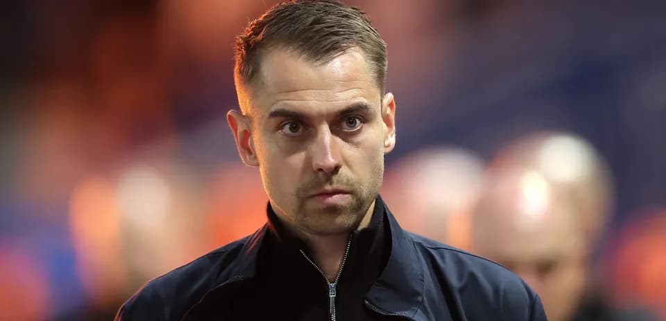 Man in dark jacket walking on stadium sidelines