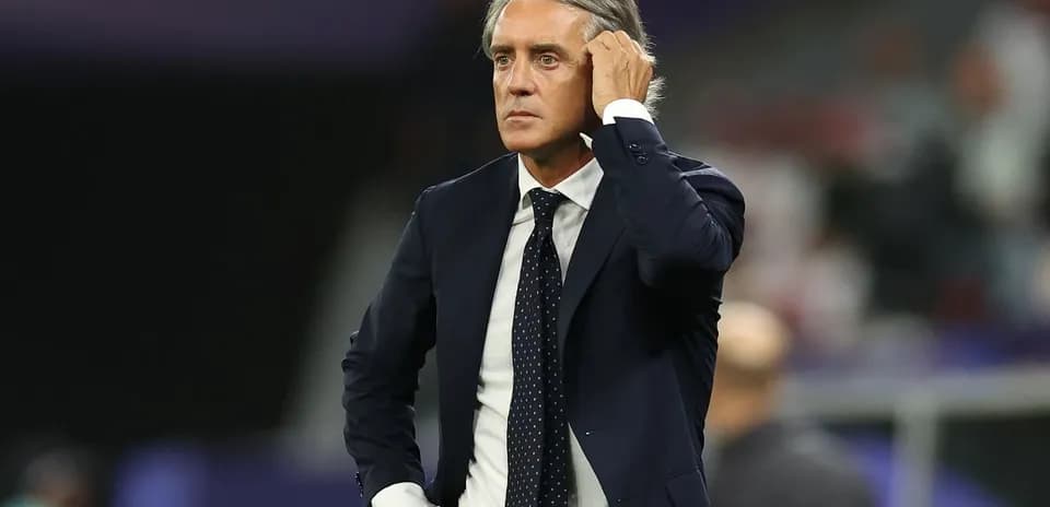 Coach observing match from sidelines with hand on head