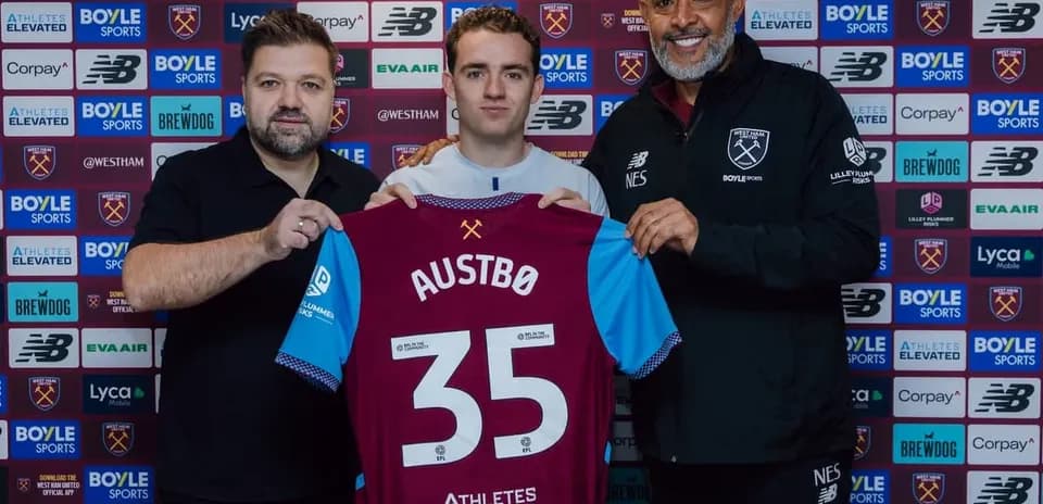 Player holding West Ham jersey with staff members