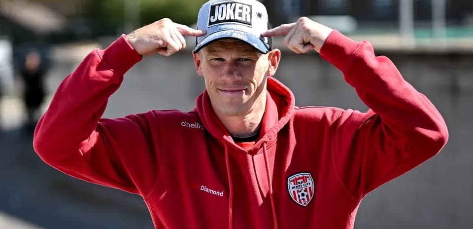 Man in red hoodie pointing at 'JOKER' cap