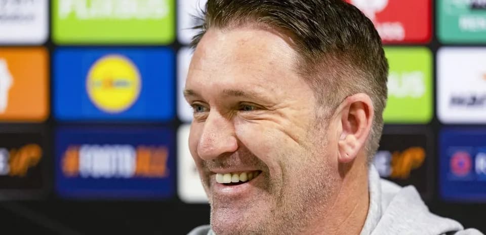 Manager smiling during press conference with sponsor backdrop