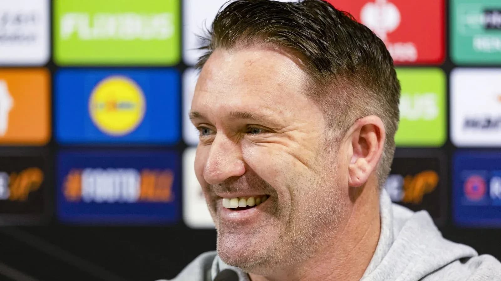 Manager smiling during press conference with sponsor backdrop
