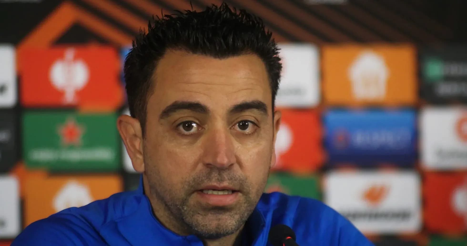 Manager speaking at press conference with logos behind
