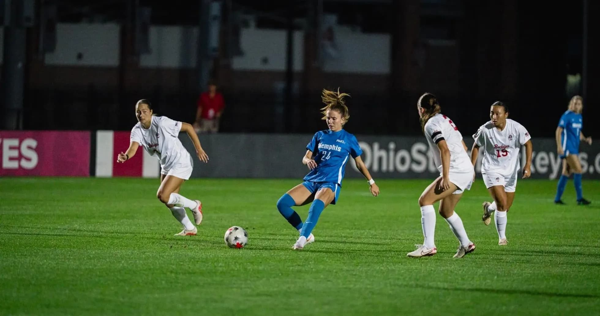 Player in blue dribbling past two defenders in white