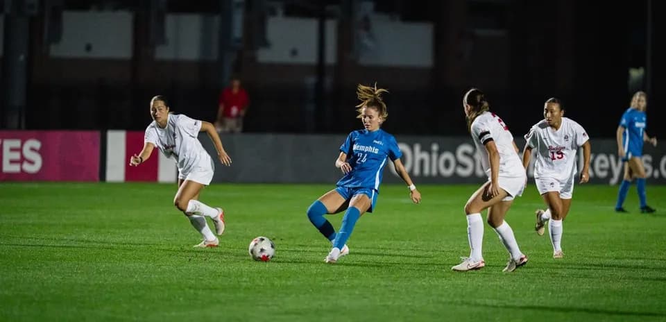 Player in blue dribbling past two defenders in white