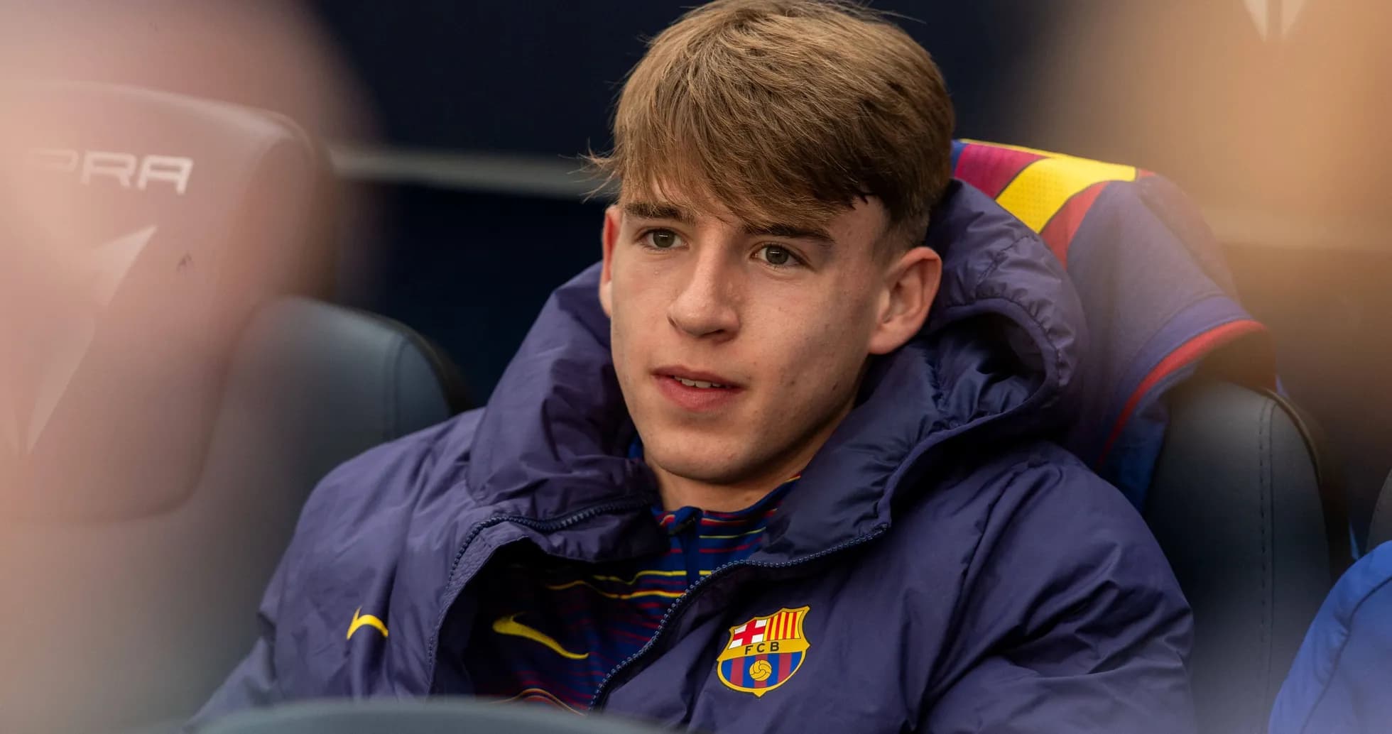 Young player seated on bench wearing Barcelona jacket Young player seated on bench wearing Barcelona jacket