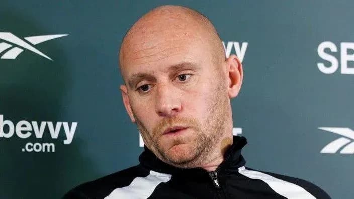 Coach speaking at press conference with serious expression Coach speaking at press conference with serious expression