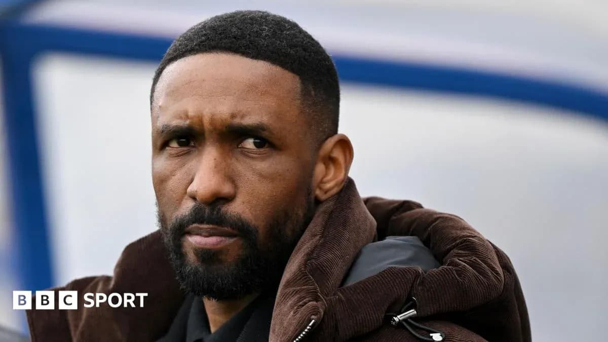Man in a brown jacket observing from sidelines Man in a brown jacket observing from sidelines