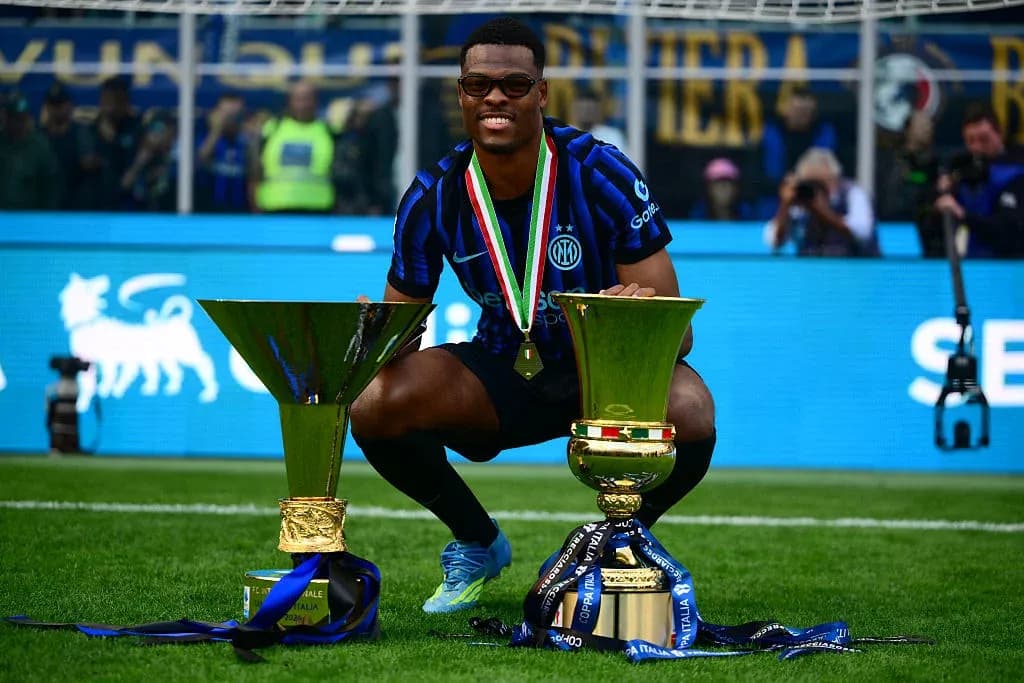 Player celebrating with two trophies on pitch Player celebrating with two trophies on pitch