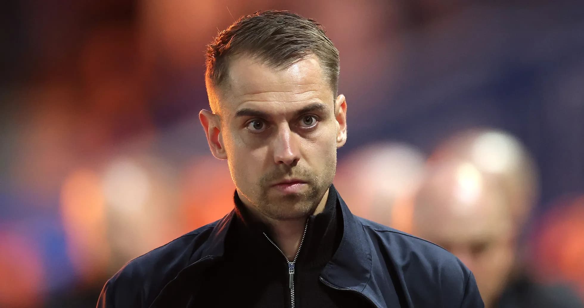 Man in dark jacket walking on stadium sidelines Man in dark jacket walking on stadium sidelines