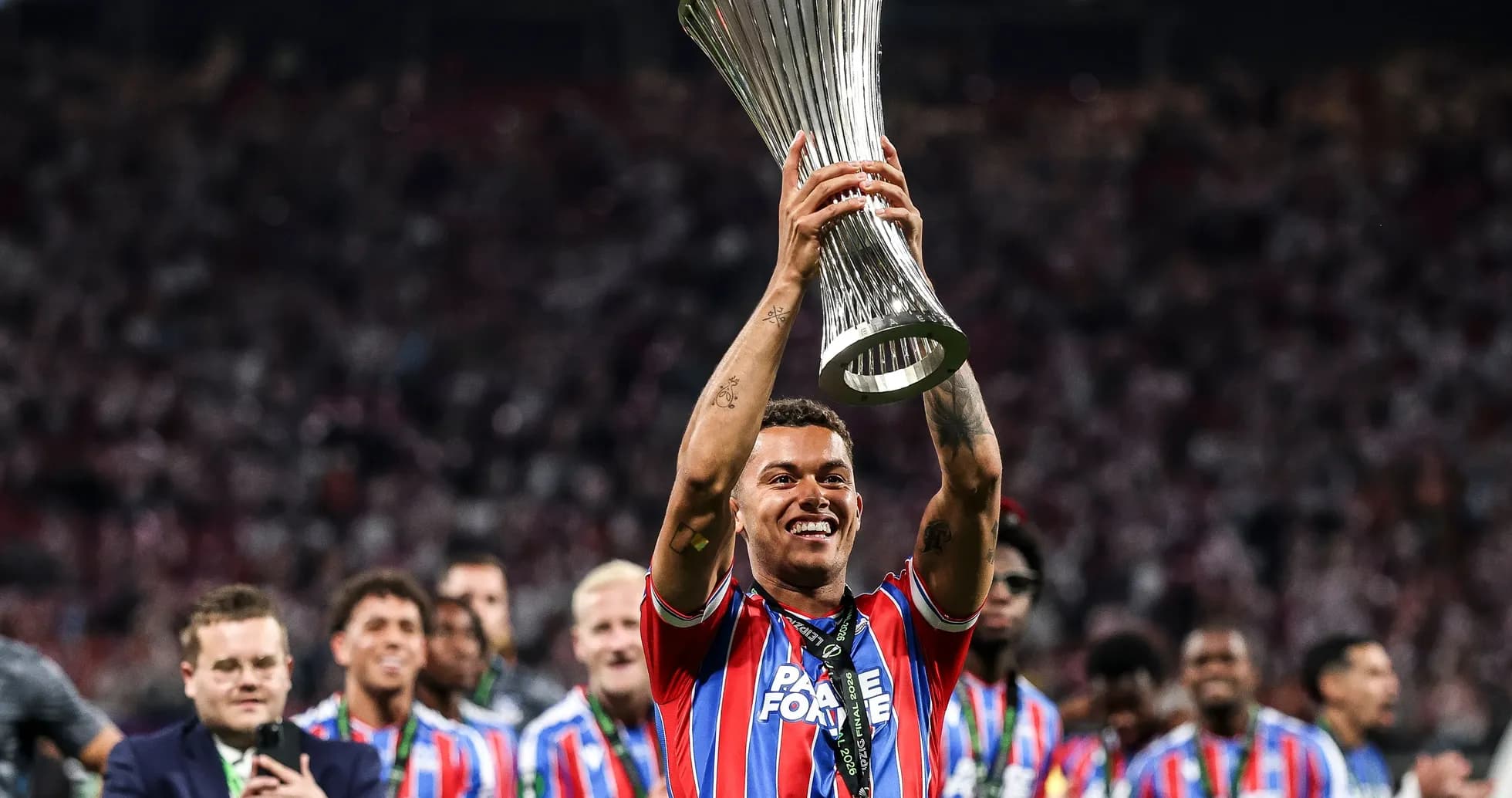Player celebrating with trophy and teammates in background Player celebrating with trophy and teammates in background